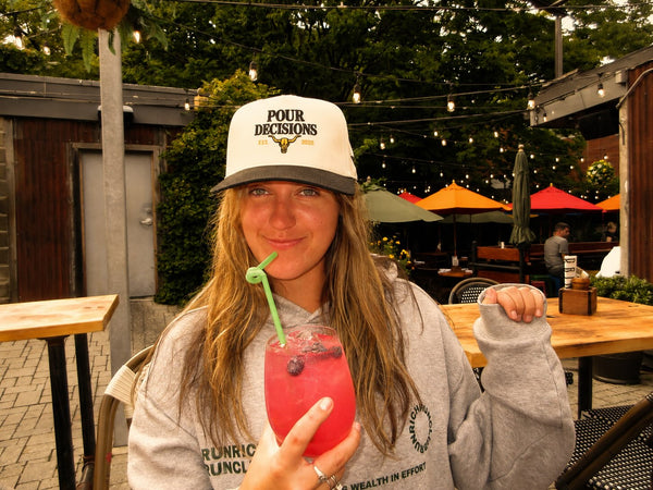 Pour Decisions SnapBack with a pink drink on a patio
